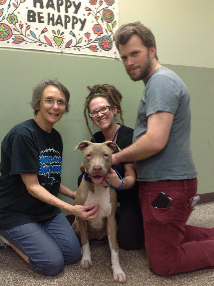 Three people and a dog are smiling for the camera.
