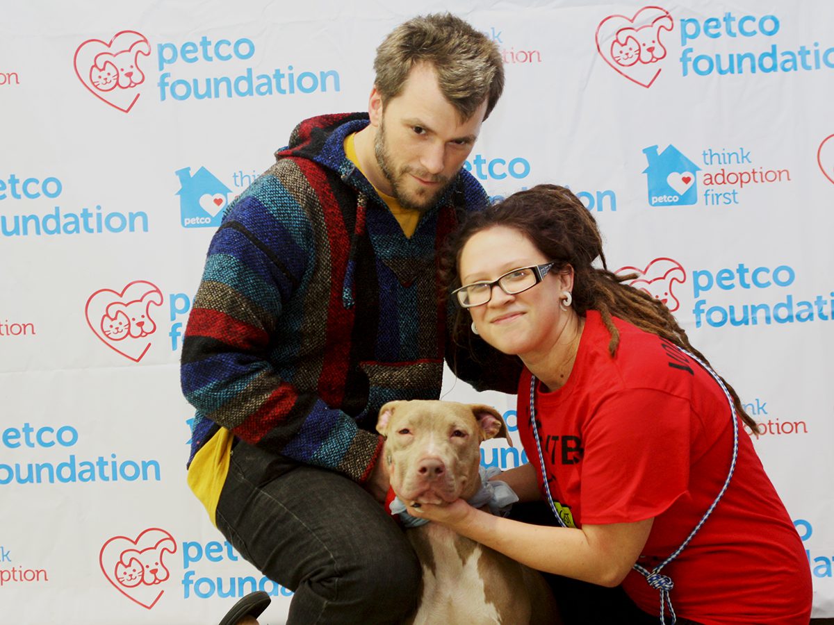 A man and woman holding a dog in front of a petco foundation sign.